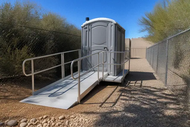 ADA-compliant portable toilet with wheelchair ramp in a gravel utility corridor in Tempe, AZ.