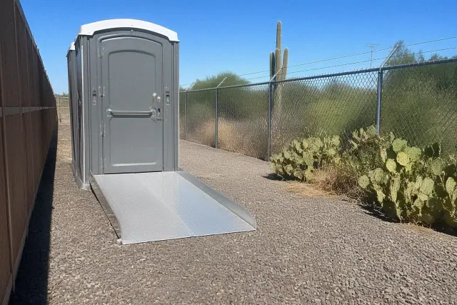 ADA-compliant portable toilet with wheelchair ramp on a gravel utility path in Scottsdale, AZ.