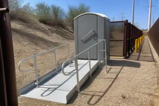 ADA-compliant portable toilet with an extended ramp in a gravel utility corridor in Phoenix, AZ.