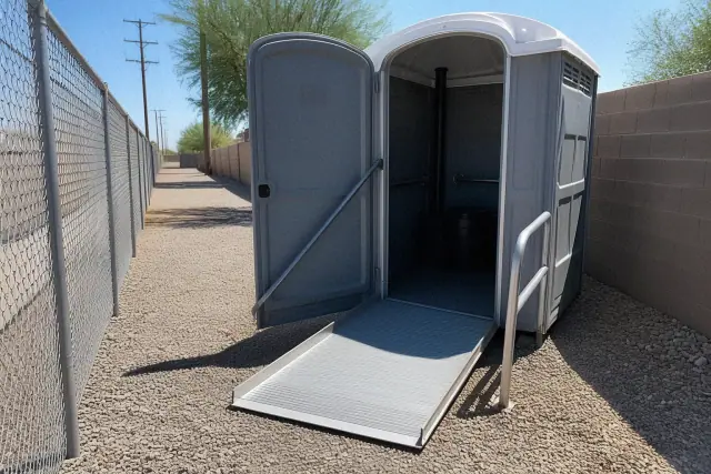ADA-compliant portable toilet with ramp access on a gravel utility path in Phoenix, AZ.