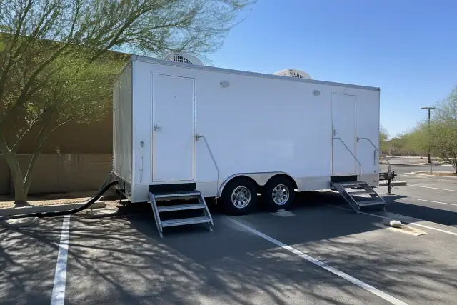 Luxury restroom trailer installed on a paved parking lot in Phoenix, AZ with visible utility hoses and power cables.