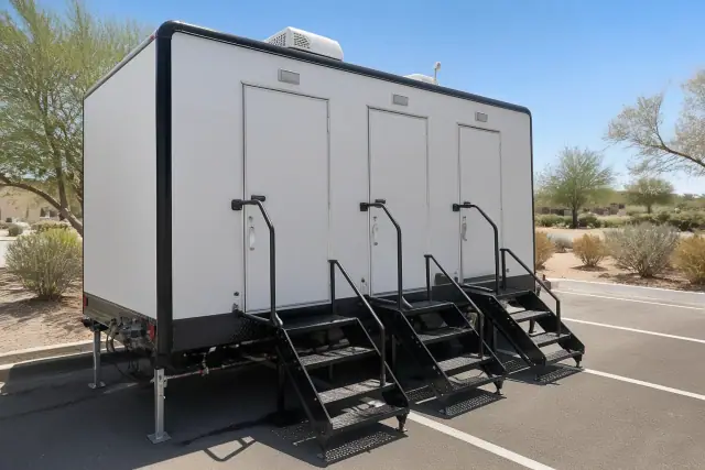 A luxury shower trailer installed on an asphalt lot in Phoenix, AZ, showing leveling jacks and plumbing connections.