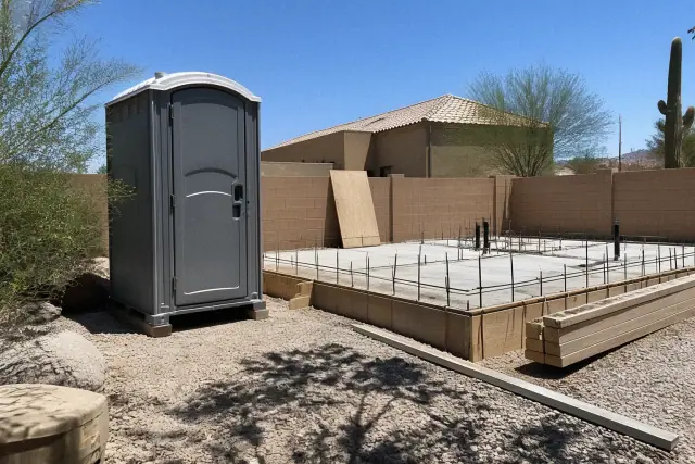 Portable construction toilet on a concrete slab at a jobsite in Mesa, AZ, with desert landscaping in harsh sunlight.