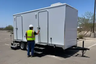Crew member inspecting a luxury restroom trailer on an asphalt parking lot in Phoenix, AZ.