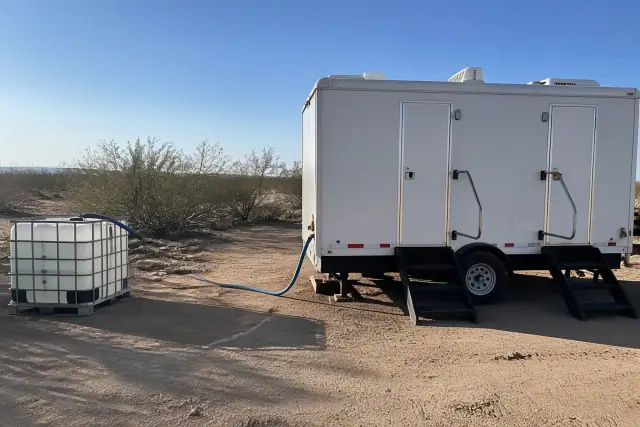 Portable shower trailer at a construction site in Phoenix, AZ, with desert soil and creosote bushes in the background.