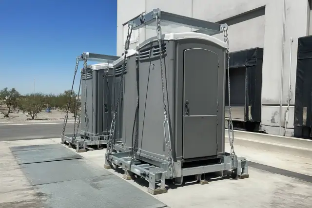 Crane-lift ready portable toilet units secured with steel cabling on a concrete loading dock in Phoenix, AZ.