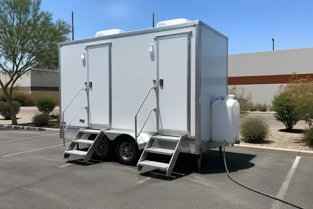Luxury restroom trailer with a water tank connection on an asphalt jobsite in Phoenix, AZ, near desert xeriscaping.