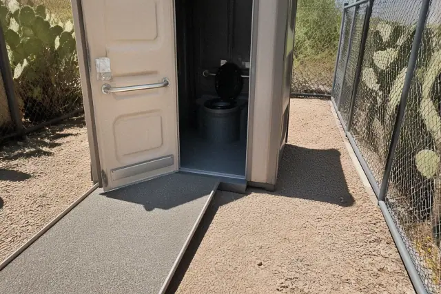 ADA-compliant portable toilet with an extended ramp in a gravel utility corridor in Phoenix, AZ.