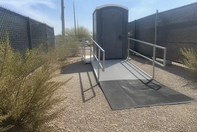 ADA-compliant portable toilet with an extended ramp in a gravel utility corridor in Phoenix, AZ.