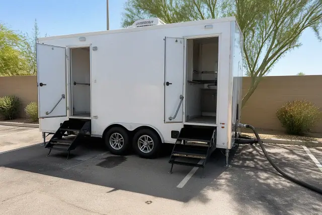 Luxury restroom trailer parked on an asphalt lot in Phoenix, AZ, with hose connections visible.