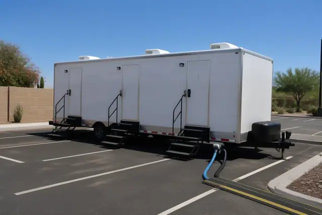 Luxury restroom trailer parked on an asphalt lot with utility hoses connected in Phoenix, AZ.