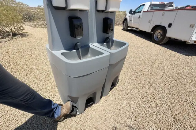 Dual handwashing station with a foot-pump water stream on a crushed stone surface at a jobsite in Buckeye, AZ.