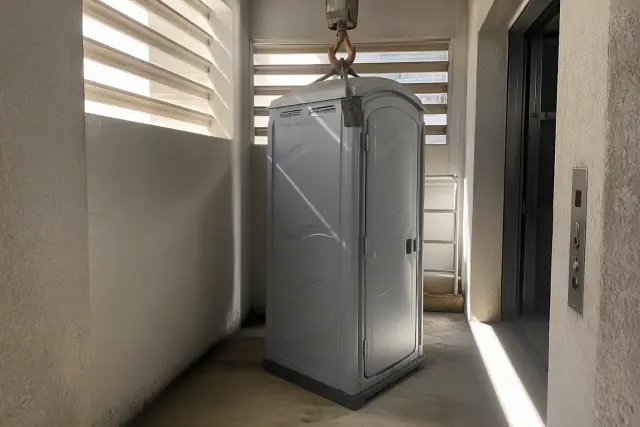 Narrow-profile portable restroom unit inside a construction service lift bay in Surprise, AZ.