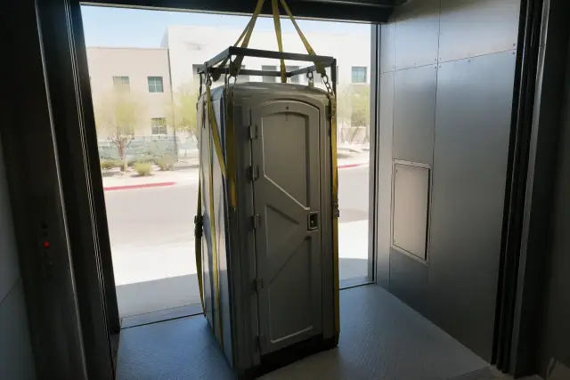 Portable restroom unit with hoisting straps secured in a service lift bay at a worksite in Glendale, AZ.