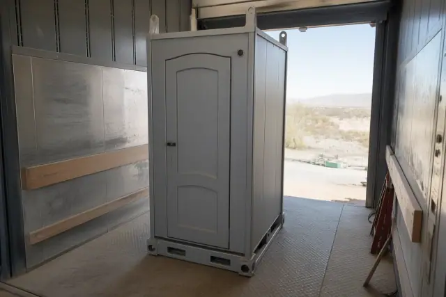 Portable restroom unit with crane brackets in an industrial service lift bay at a jobsite in Scottsdale, AZ.