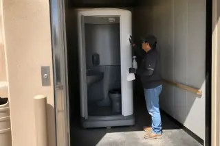 Technician cleaning the interior of a portable restroom unit in a freight elevator at a Phoenix, AZ worksite.