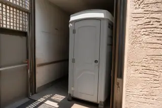 Narrow-profile portable restroom unit in an industrial service lift bay in Phoenix, AZ.