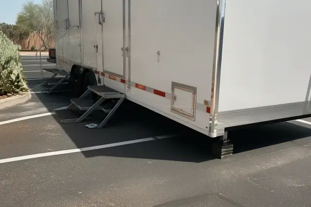 Luxury restroom trailer placed on an asphalt parking lot in Gilbert, AZ, with desert landscaping nearby.