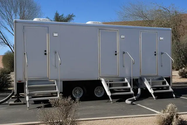Luxury restroom trailer on a parking lot in Glendale, AZ with waste hoses and leveling blocks.