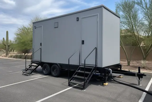 Standard portable toilet rental on an asphalt parking lot in Goodyear, AZ with leveling shims and a waste hose.