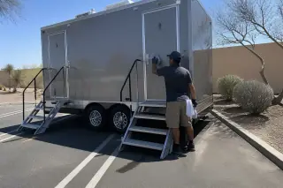 Worker sanitizing the door of a luxury restroom trailer on a paved parking lot in Phoenix, AZ.