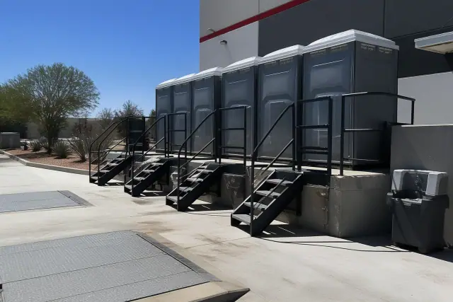 A row of portable toilets on a concrete loading dock at an industrial site in Phoenix, AZ.
