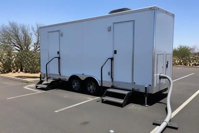 Luxury restroom trailer parked on an asphalt lot with prickly pear cacti in the background in Mesa, AZ.