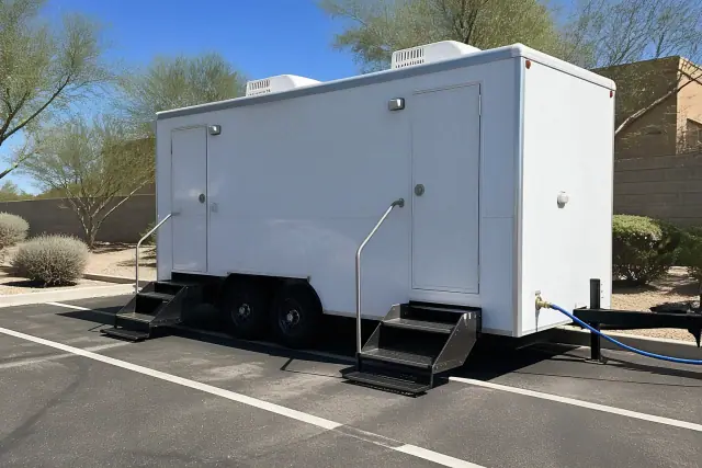 Luxury restroom trailer parked on asphalt in Chandler, AZ with a water hose connected to the base.