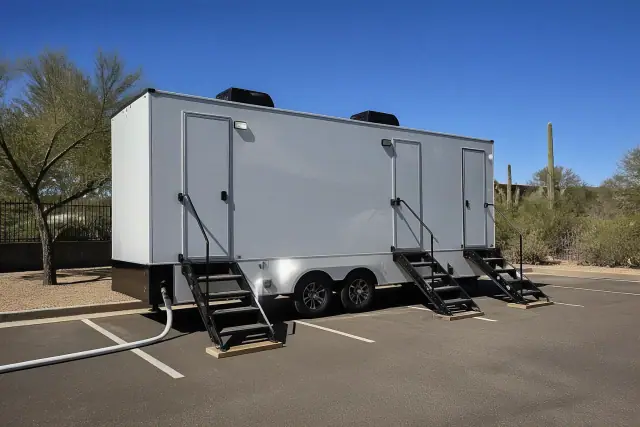 Luxury restroom trailer parked on asphalt with stairs and utility hose in Scottsdale, AZ.