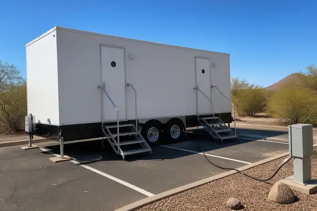 Luxury restroom trailer parked on asphalt in Buckeye, AZ, with visible leveling jacks and a power cable connection.