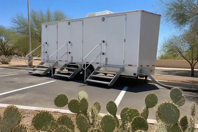 Luxury restroom trailer parked on asphalt in Tempe, AZ, with white steps and a sewer hose in a desert setting.