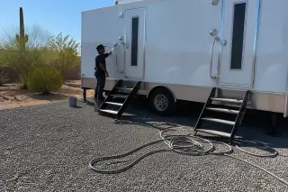 Technician cleaning a luxury restroom trailer handle on a crushed stone lot in Phoenix, AZ.