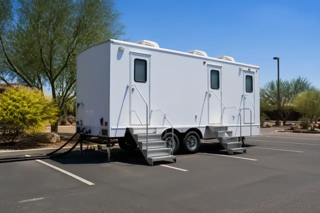 Luxury restroom trailer installed on an asphalt lot with leveling jacks and utility hoses in Phoenix, AZ.
