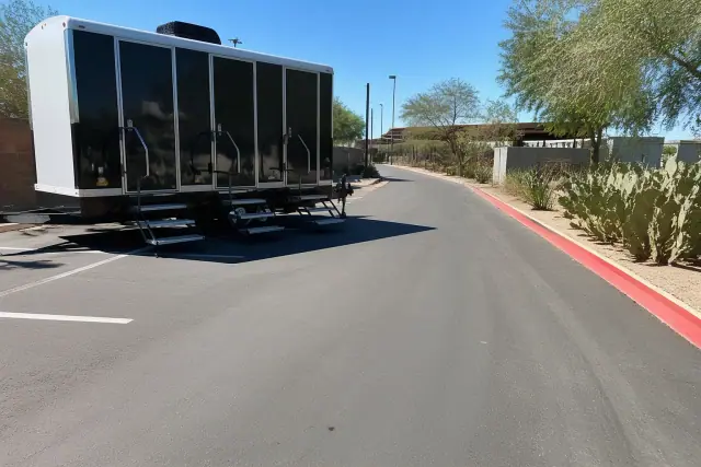 Luxury restroom trailer parked on an asphalt service route with prickly pear cactus landscaping in Phoenix, AZ.