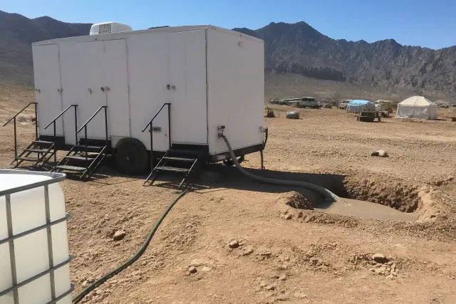 Portable shower trailer connected to a water hose on a dirt lot in Surprise, AZ.