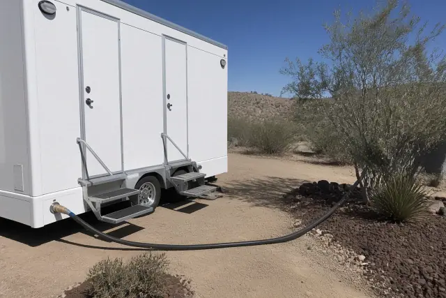 Portable shower trailer on a dirt lot with a water hose connection in Mesa, AZ.