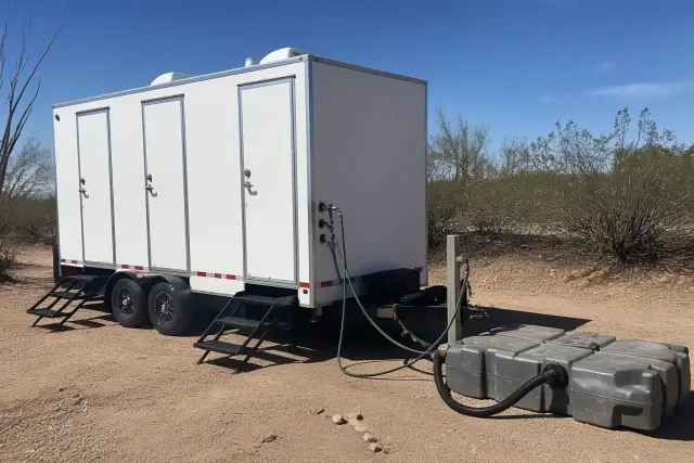 Portable shower trailer connected to a water supply and waste tank on a desert site in Tempe, AZ.
