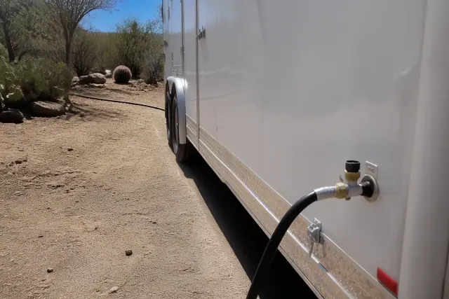 Portable shower trailer connected to a water hose in a xeriscape desert clearing in Scottsdale, AZ.