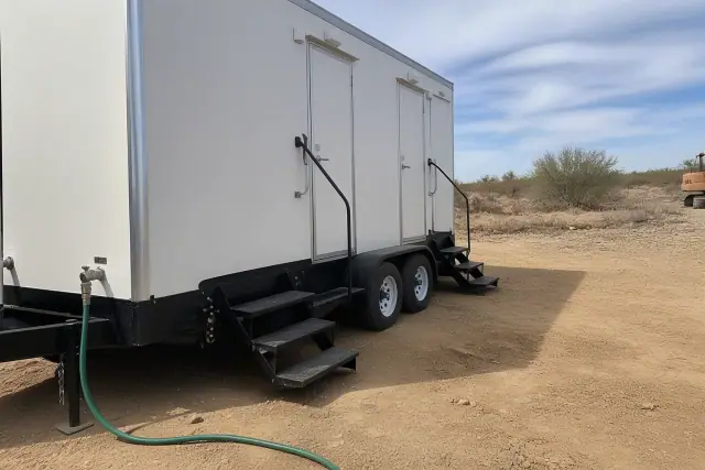 Portable shower trailer connected to a water hose on a dirt site in Buckeye, AZ.