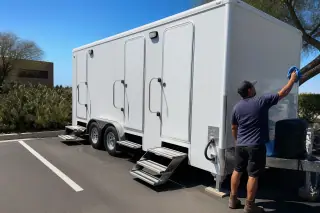 Contractor cleaning a luxury restroom trailer on a marked asphalt parking lot in Phoenix, AZ.