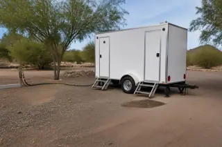 Portable shower trailer connected to a water supply on hard-packed desert soil in Phoenix, AZ.