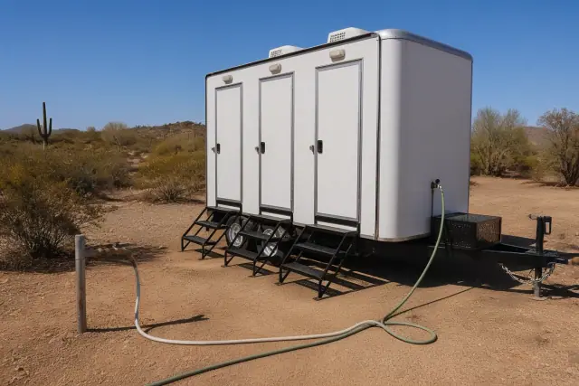 Portable shower trailer connected to a water supply line on a dirt worksite in Phoenix, AZ.