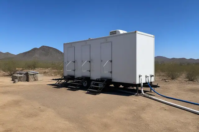 Portable shower trailer installed on a dirt jobsite in Phoenix, AZ, showing water and drainage connections.