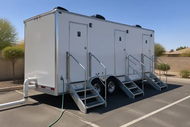 Luxury restroom trailer parked on asphalt in Chandler, AZ with visible water hose and waste vent.