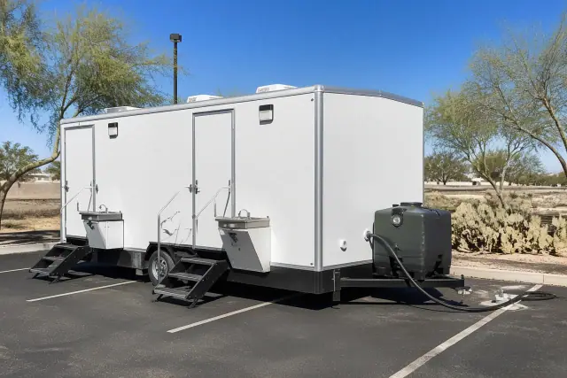 Portable toilets with sinks placed on an asphalt parking lot in Goodyear, AZ with desert cacti in the background.