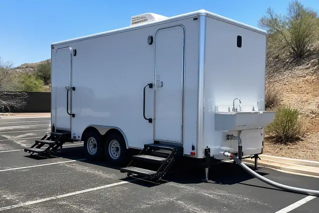 Portable restroom trailer with an exterior sink and water hose parked on an asphalt lot in Mesa, AZ.