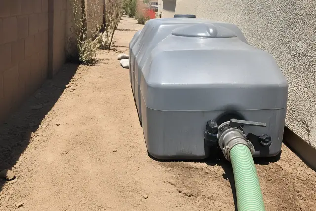 Portable waste holding tank with industrial hose in a side yard utility path in Gilbert, AZ.