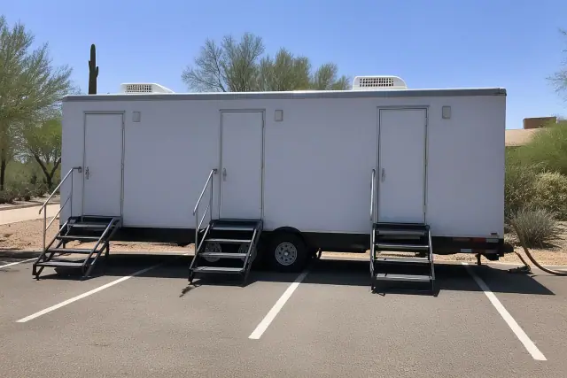 Luxury restroom trailer parked on an asphalt lot with desert vegetation in Phoenix, AZ.