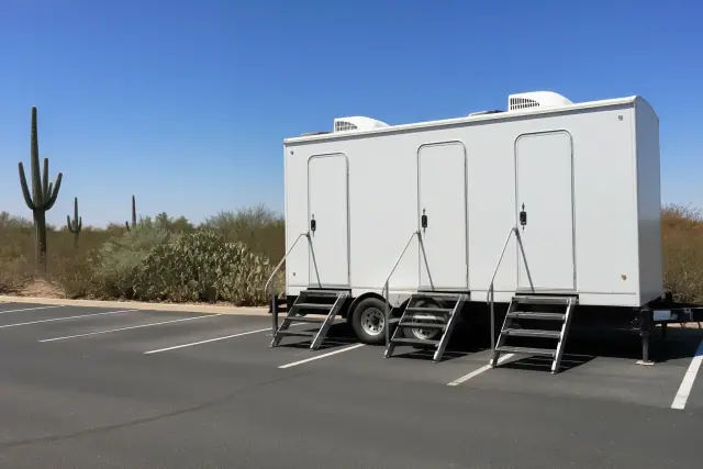 Luxury restroom and shower trailer parked on an asphalt lot in Phoenix, AZ, with desert cacti in the background.