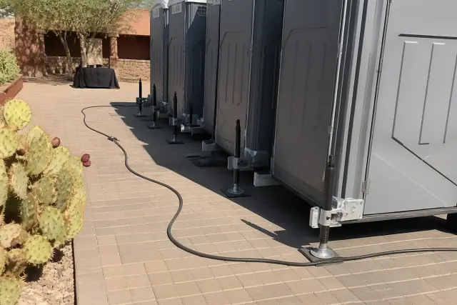 Portable toilets arranged on a paved courtyard in Goodyear, AZ with leveling jacks and electrical cables visible.